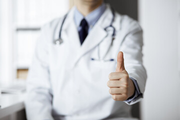 Unknown male doctor sitting with thumbs up sign at his working place in clinic, closeup. Perfect...