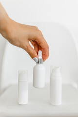 a woman's hand opens a white serum bottle on a white background