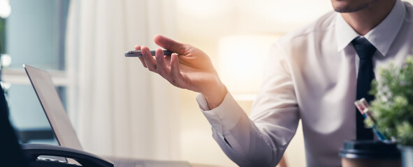 Businessman sitting at the desks with holding a pen and point it forward. Computers and phones on the table in the modern office.