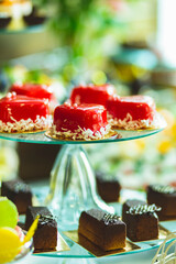 Small cakes in the shape of a heart are covered with red icing. Original heart-shaped desserts. Different sort of beautiful pastry, small colorful sweet cakes. 