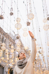 A man in a white knitted sweater on the street in winter reaches for a garland