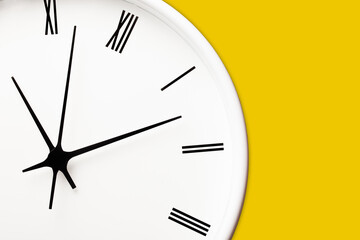 White round clock with black arrows and numbers on yellow wall. Time symbol background.	Hours and minutes texture. Empty copy space isolated clock. Daily hourly routine backdrop.