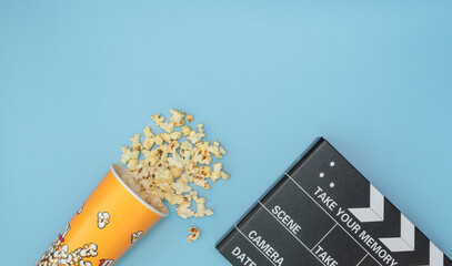 Popcorn cup and movie clapper board on blue background. Movie night concept. Flat lay style with copy space.