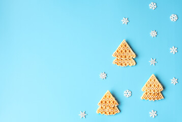 Christmas trees made of Belgian waffles with white beads on blue background with white snowflakes. Winter card. Cooking at home concept. Flat lay style with copy space for your text.