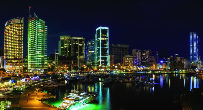 A panoramic photo of Beirut, Lebanon city skyline at night, featuring the vibrant neon lights of the marina with boats and a scenic waterfront walk.	