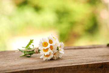 Small bunch of chrysanthemum flowers tied with brown string on wooden surface with green bokeh background