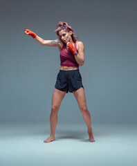 Female fighter trains in boxing bandages in studio on gray background.