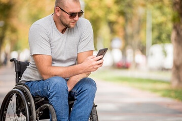 Handicapped man in wheelchair at the park alley use a smartphone