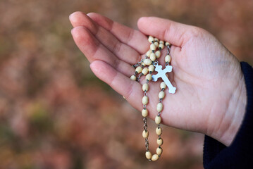 Women's hands holding rosary at the autumn background.