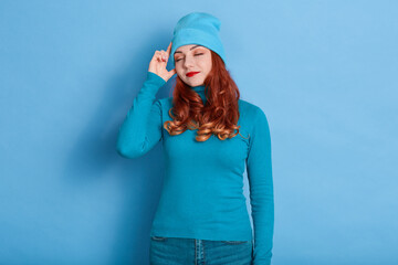 Red haired young adult woman calm face and keeps index fingers on temple, tries to remember...