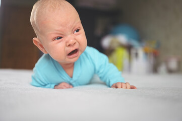 Cute emotional funny newborn infant crying boy laying on bed. Infant baby facial expressions.