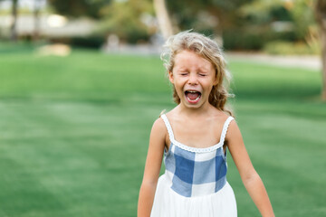 Beautiful sad little blonde curly hair girl crying, on summer background. Concept relationships with children and friendship in school and babygarden .Child crisis .Copy space