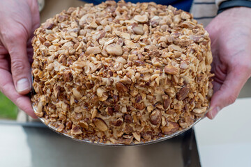 Mans hand holding nut biscuit cake finished with crushed sugar-coated candied caramelized almonds