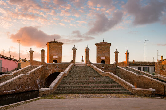 Comacchio, Ferrara / Italy - August 2020: Trepponti Bridge in Comacchio at dawn with a tourist in the center of the columns, sky with clouds