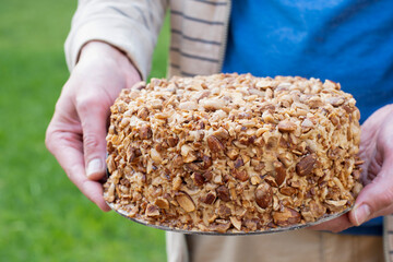 Mans hand holding nut biscuit cake finished with crushed sugar-coated candied caramelized almonds