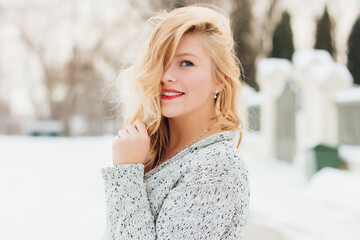 Portrait of a young woman in a sweater blonde walks around the city on a snowy day