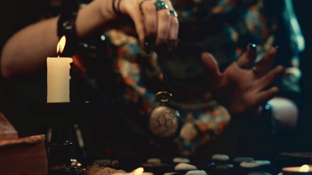Divination and magic. A fortune teller conjures an amulet over scattered runes. Close-up of hands with dark manicure and rings