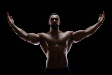 Fototapeta na wymiar Portrait of a bodybuilder standing isolated on black background in a shadow with raised hands to show off his muscles