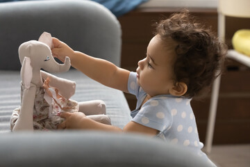 Cute little african American baby play with stuffed toy in cozy children room at home. Small biracial toddler child have fun engaged in funny game with plush animal indoors. Childcare concept.