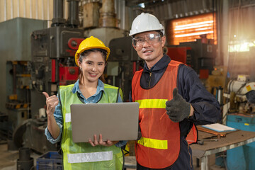 Portrait of female engineer and male worker showing thumb up. A successful team of technician and foreman use a laptop to control lathe machine in metalwork factory. Workplace gender equality concepts