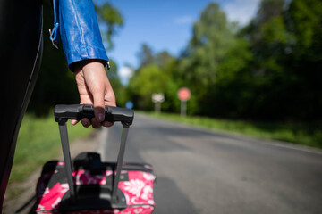 A young female hand holds a black handle from a pink suitcase on wheels and everything seen up close.