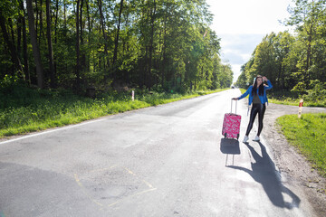 A teenager is standing with a pink suitcase on wheels and tries to stop the opportunity to go on vacation faster.