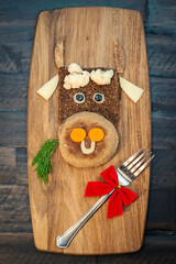 Funny food with edible symbol of 2021 bull cow made from bread, cheese and vegetables. Breakfast idea for kids. New Year Christmas food top view. Holiday, celebration, art food.