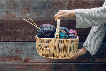 Wicker basket with colorful bright balls of wool yarn for knitting in female hands. Knitting yarn,...
