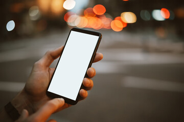 Close-up of male hands with smartphone on night street. Empty blank screen. Mock-up