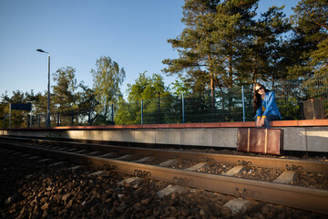 A teenager is sitting in a forbidden place on a railway platform and her legs are hanging over the...