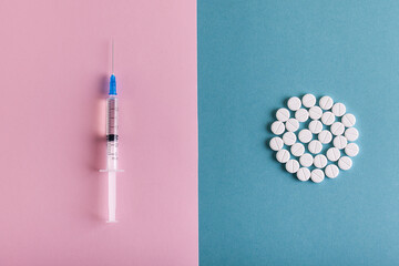 Syringe and white tablets on blue pink background. Corovirus concept. Covid-19 concept.