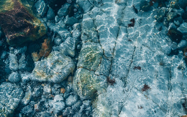 Top view of stones under transparent sea ocean blue clean water surface with refractions