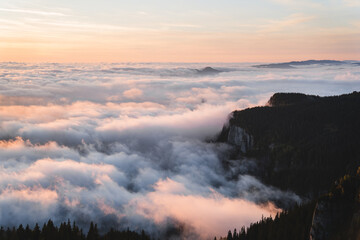 Stunning top view with mist over forest and mountains at sunrise.  Colorful landscape with forest in low clouds, mountains peaks above fog, orange sky with sun in the morning in fall. Top view. Nature