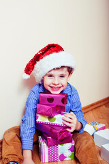 little cute boy with Christmas gifts at home wearing red Santas hat. closeup emotional happy smiling in mess with toys, lifestyle holiday people concept
