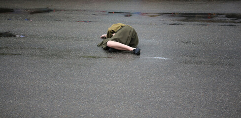 Young woman lying down on ground. Sick or ill girl unconscious outside on the wet asphalt. Victim...