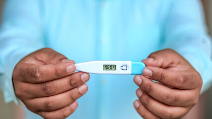 Man holds digital thermometer with temperature reading in Fahrenheit closeup.