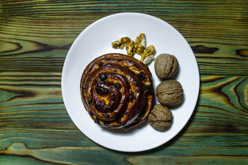 Fragrant bun with raisins and nuts on a white plate on a green wooden background