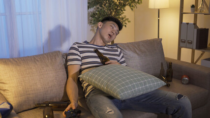 exhausted asian chinese guy gamer playing game until late night and felling asleep on couch while...