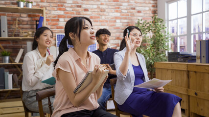 Photo of elegant pregnant listener raising hand to ask question while four asian man and women sitting on chair and taking new employee training lesson in office together.