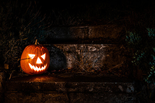 Spooky Halloween pumpkin lantern on concrete stairs in the garden at night