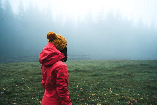 Dressed bright red jacket young female hiker looking for directions in autumn foggy forest. Active people and autumnal moody vacation time spending concept image