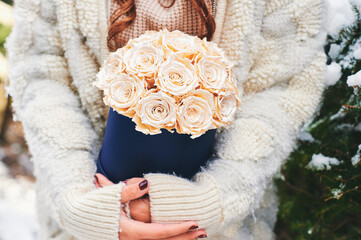 Outdoor portrait of beautiful woman holding  box with golden roses, wearing knitted jacket