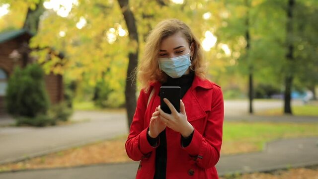Social distancing, online video chat, woman in surgical mask call his friend at the autumn park