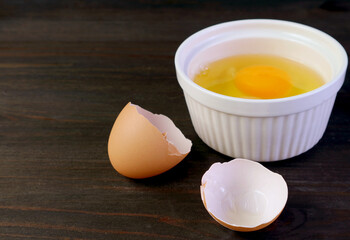 Closeup cracked eggshell on dark brown wooden table with blurry raw egg bowl in background