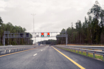 Road view with speed limit signs through windshield car window with going rain drops during driving at speed. Unfocused highway. Autumn