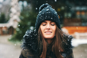 Seasonal outdoor portrait of happy young woman enjoying nice sunny winter day, eyes closed