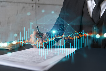 Businessman in suit signs contract. Double exposure with forex graph hologram. Man signing...