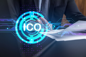 Businessman in suit signs white papper. Double exposure with ICO icon hologram. Man signing contract agreement. Blockchain market analysis and investment concept.