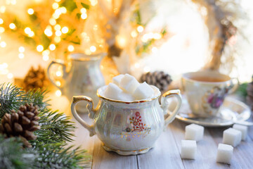 Mother-of-pearl sugar bowl from an antique porcelain set with refined sugar. Christmas breakfast on the background of garlands and fir branches.