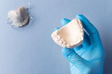 dentist's hand in blue glove holding plaster cast of children's jaw over blue background with...